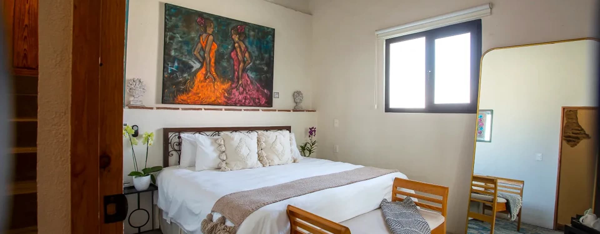 King bed with a wrought-iron headboard and a timber bench at the foot, under beams, with a painting of two dancers on the wall