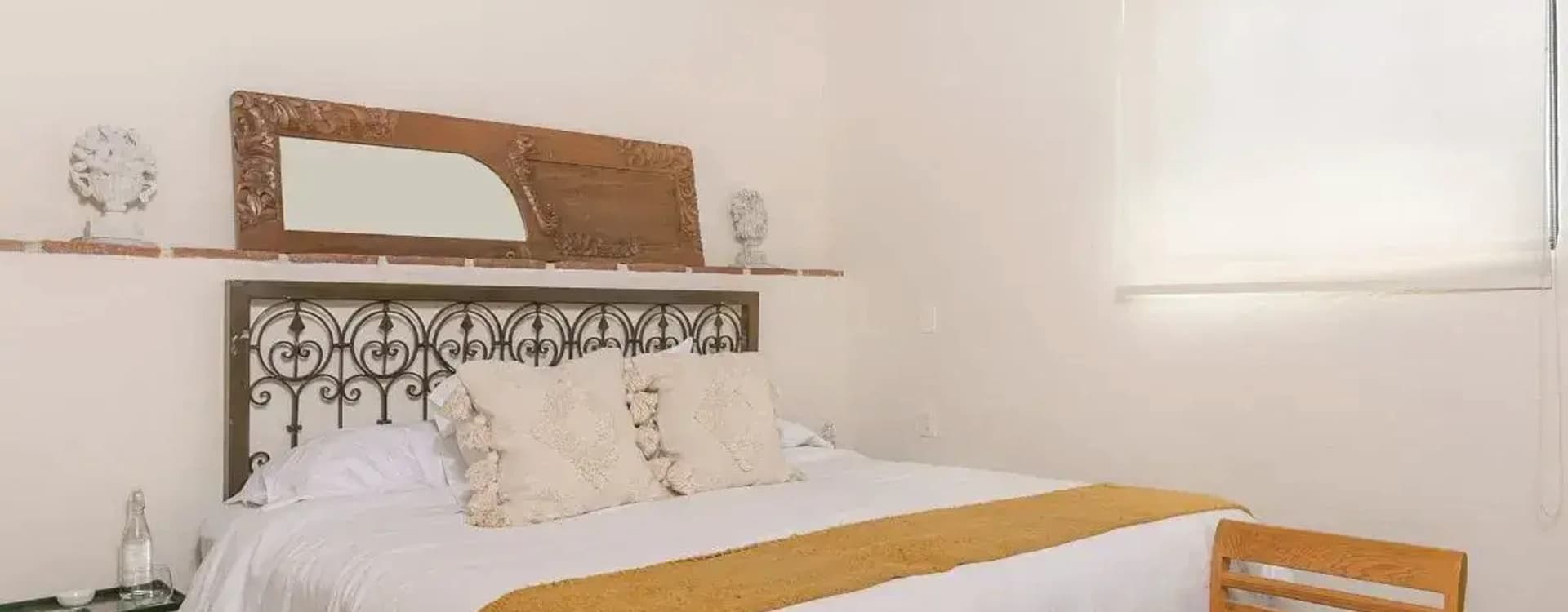 King bed with a wrought-iron headboard, an antique carved mirror on the ledge and a mustard runner