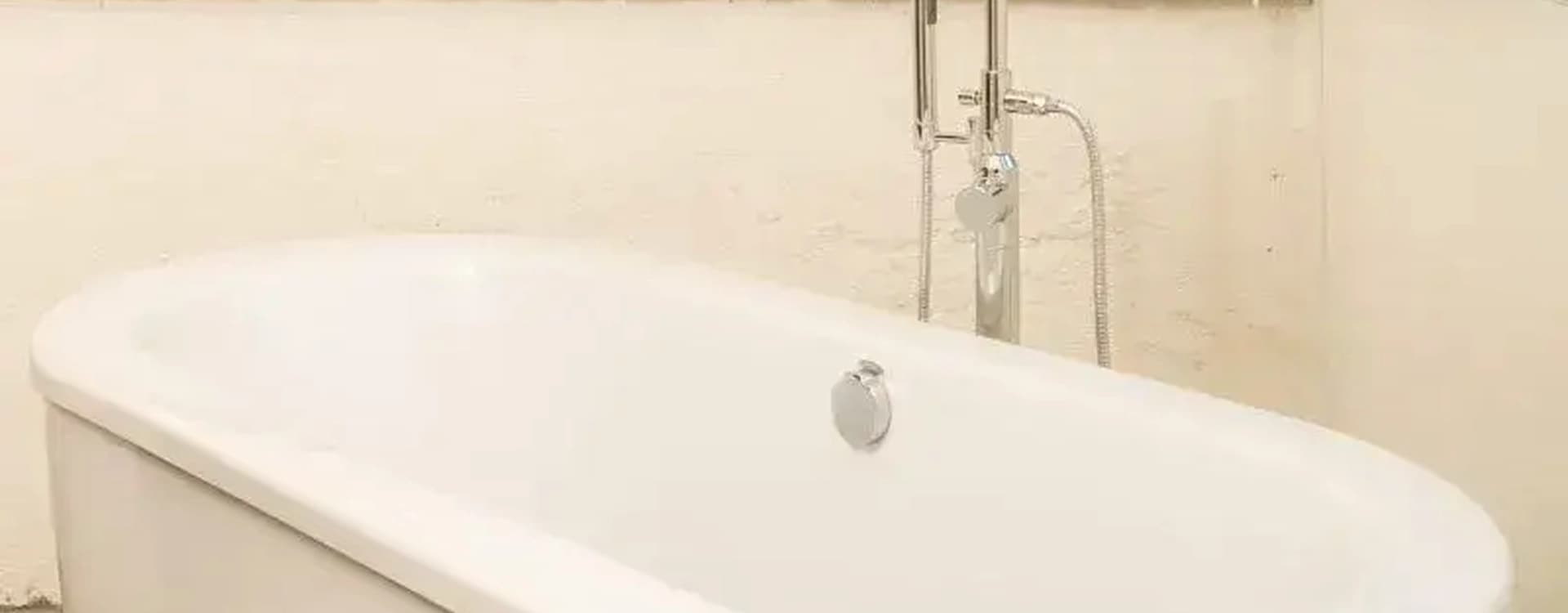 Freestanding white bathtub beside a window, with a niche in the wall and dried branches on the ledge