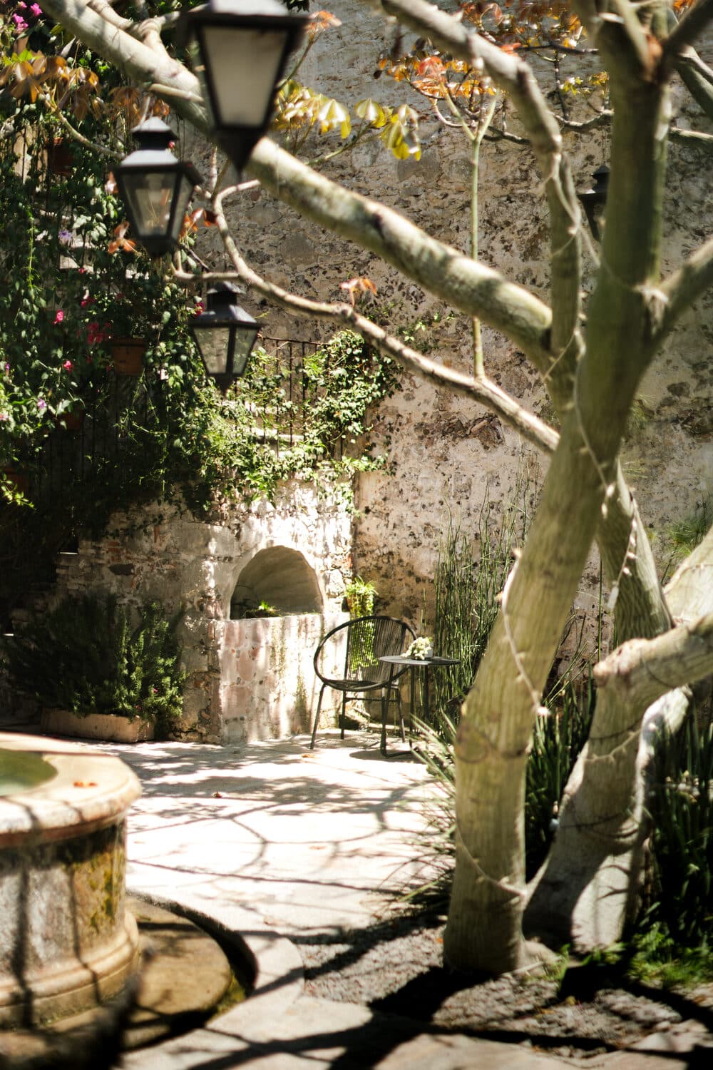 The courtyard with iron lanterns hanging from a tree, a stone wall with a low arch and bougainvillea