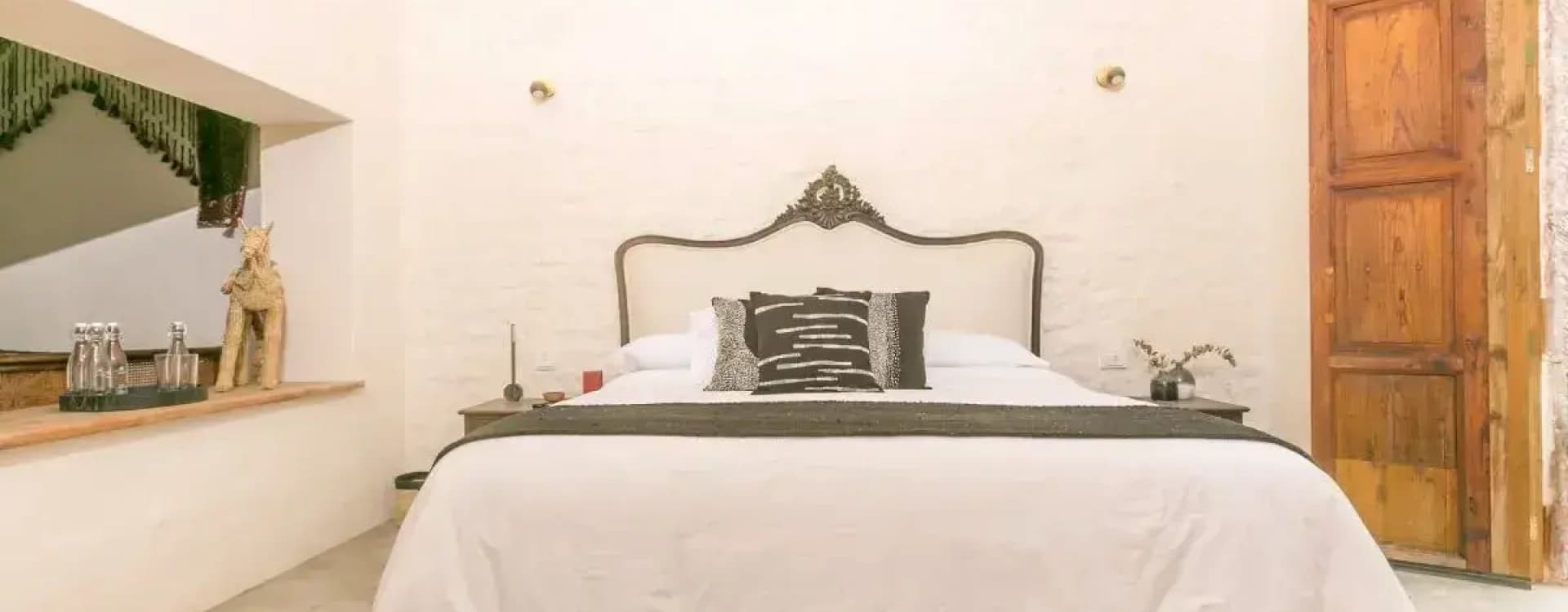 Front view of the king bed with an upholstered headboard and a carved crest, between two brass sconces