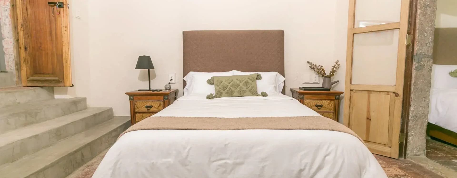 Bed with an upholstered headboard between two timber nightstands, with a lamp and stone steps to one side