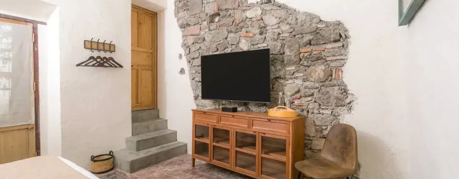 Timber cabinet with a television on an exposed stone wall, beside the timber door and the steps