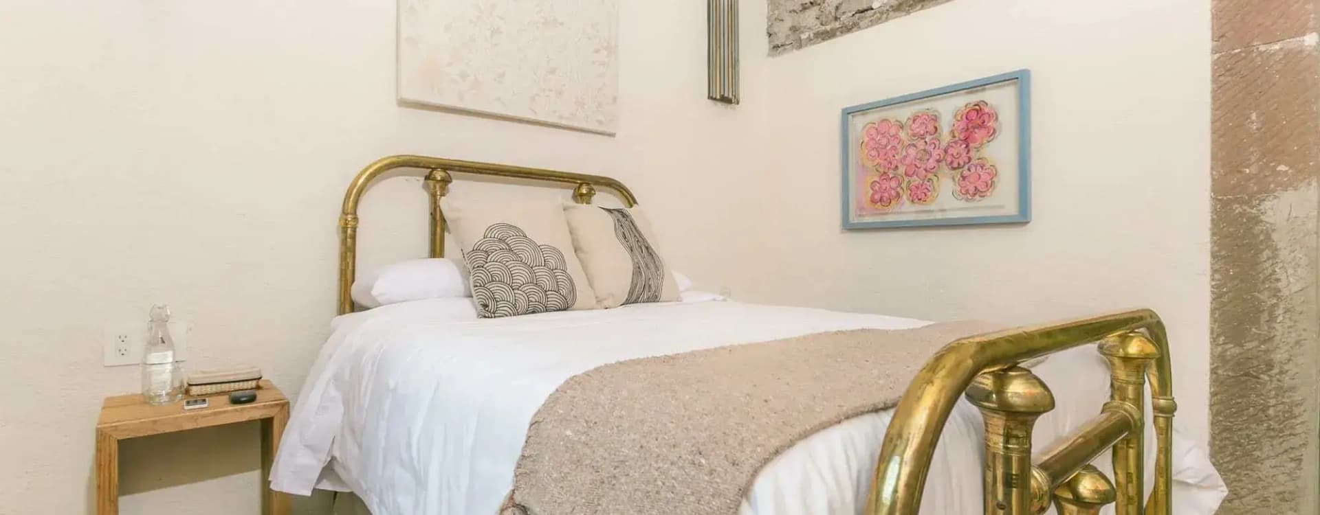 Detail of the brass bed with a wool runner, beneath a watercolour of flowers and a stone wall