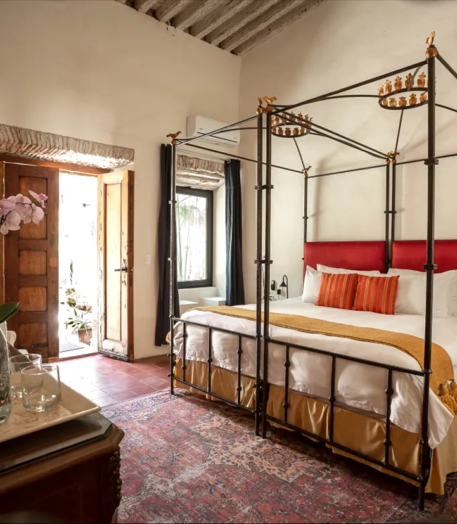 Suite with a wrought-iron four-poster king bed and a red headboard, under timber beams and beside the door to the patio