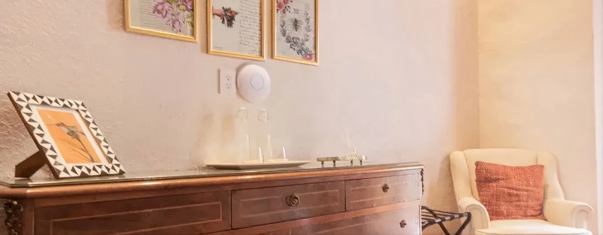 Antique timber dresser with three framed prints and a cream armchair in the corner
