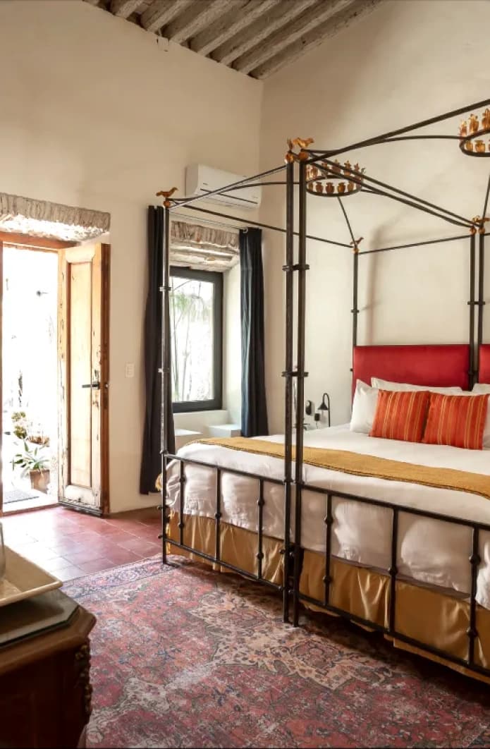 Suite with a wrought-iron four-poster king bed and a red headboard, under timber beams and beside the door to the patio